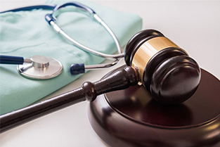 A gavel and soundblock on a table with a stethoscope sitting on a set of folded scrubs.